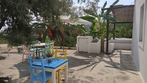Un espace extérieur aménagé en terrasse, avec une table et des chaises, entouré de verdure et bordé d’un mur blanc.