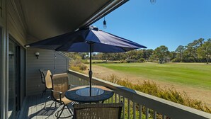 Ein Balkon mit Tisch und Stühlen, einem Sonnenschirm und Blick auf einen Golfplatz.