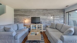 Ein modernes Wohnzimmer mit zwei grauen Sofas, einem Couchtisch, einem Fernseher auf einer Holzkommode und einem großen Fenster.