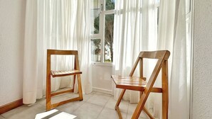 Een kamer met twee houten stoelen, een raam met witte gordijnen en uitzicht op bomen.