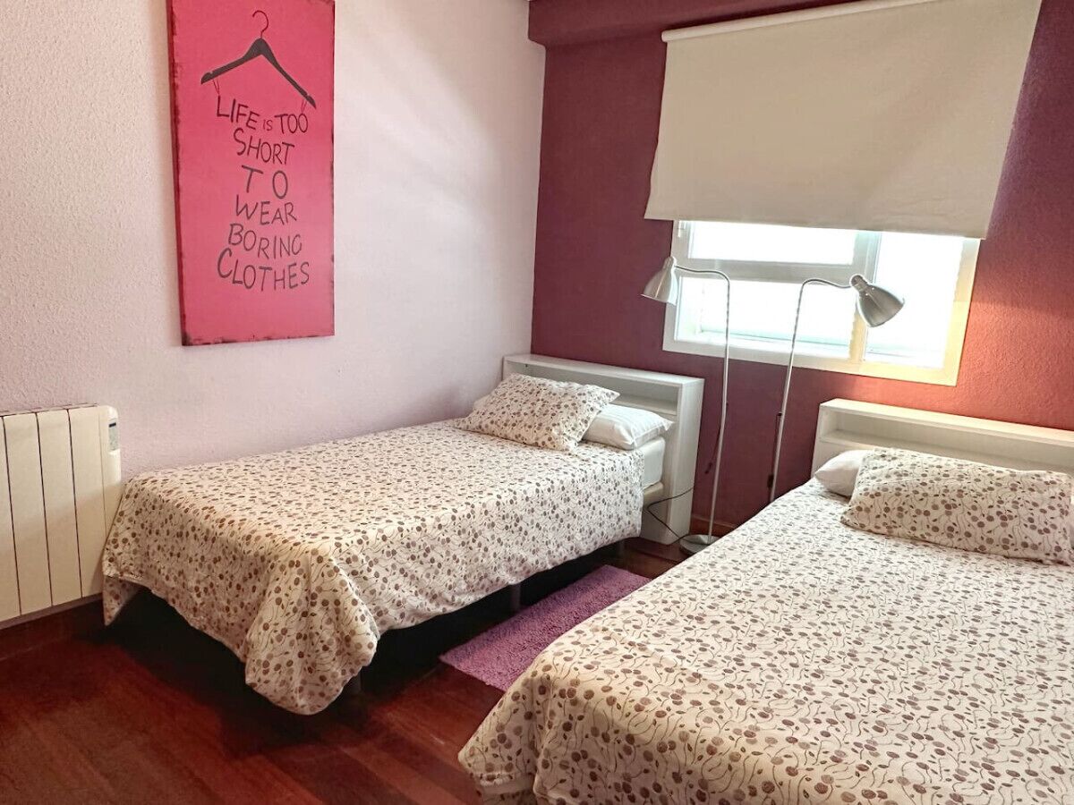 A small bedroom with two single beds, a radiator, a window with a blind, and a motivational poster on the wall.