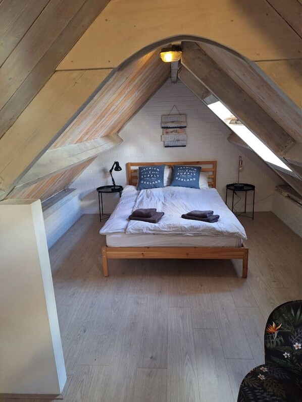 Ein Schlafzimmer mit schrägen Wänden, einem Bettgestell aus Holz, zwei Nachttischen und einer Wandleuchte.