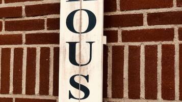 A wooden sign with "THE BEACH HOUSE" written on it, mounted on a brick wall.