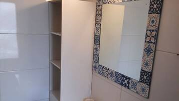A bathroom with a white sink, a mirror with a decorative frame, and a shelf unit.