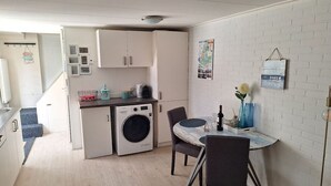 Een compacte keuken met een wasmachine, een eettafel met stoelen en een kleine koelkast.