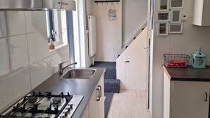 Een kleine keuken met een gasfornuis, een spoelbak en lichtgekleurde kastjes. Op het aanrecht staat een kleine koelkast en een magnetron.