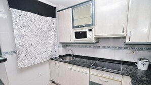 A compact kitchen with white cabinets, a black countertop, a microwave, a sink, and a dishwasher.