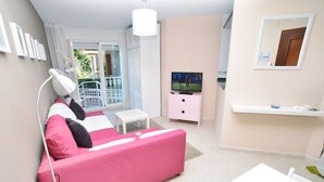 A modern living room with a pink sofa, a white lamp, a television, and a small table. - Apto con terraza y piscina - La Barrosa 5603 (Arnuero)