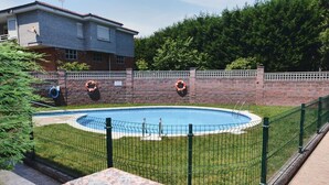 A swimming pool surrounded by a brick wall and a metal fence, with lifebuoys attached to the wall.