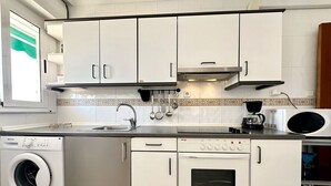 A compact kitchen with white cabinets, a built-in washing machine, an oven, and a microwave.