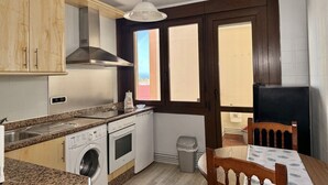 A compact kitchen with a washing machine, oven, and a dining area with a table and chairs.