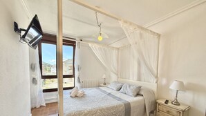 A bedroom with a bed, a bedside table, a lamp, a wall-mounted TV, and a window with curtains.
