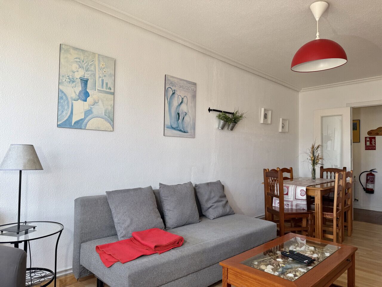 A living room with a grey sofa, a red throw blanket, a wooden dining table, and a red pendant light.