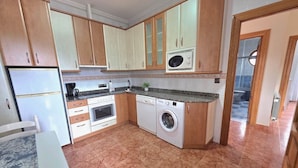 A compact kitchen with wooden cabinets, a microwave, a washing machine, and a dining area with a table.