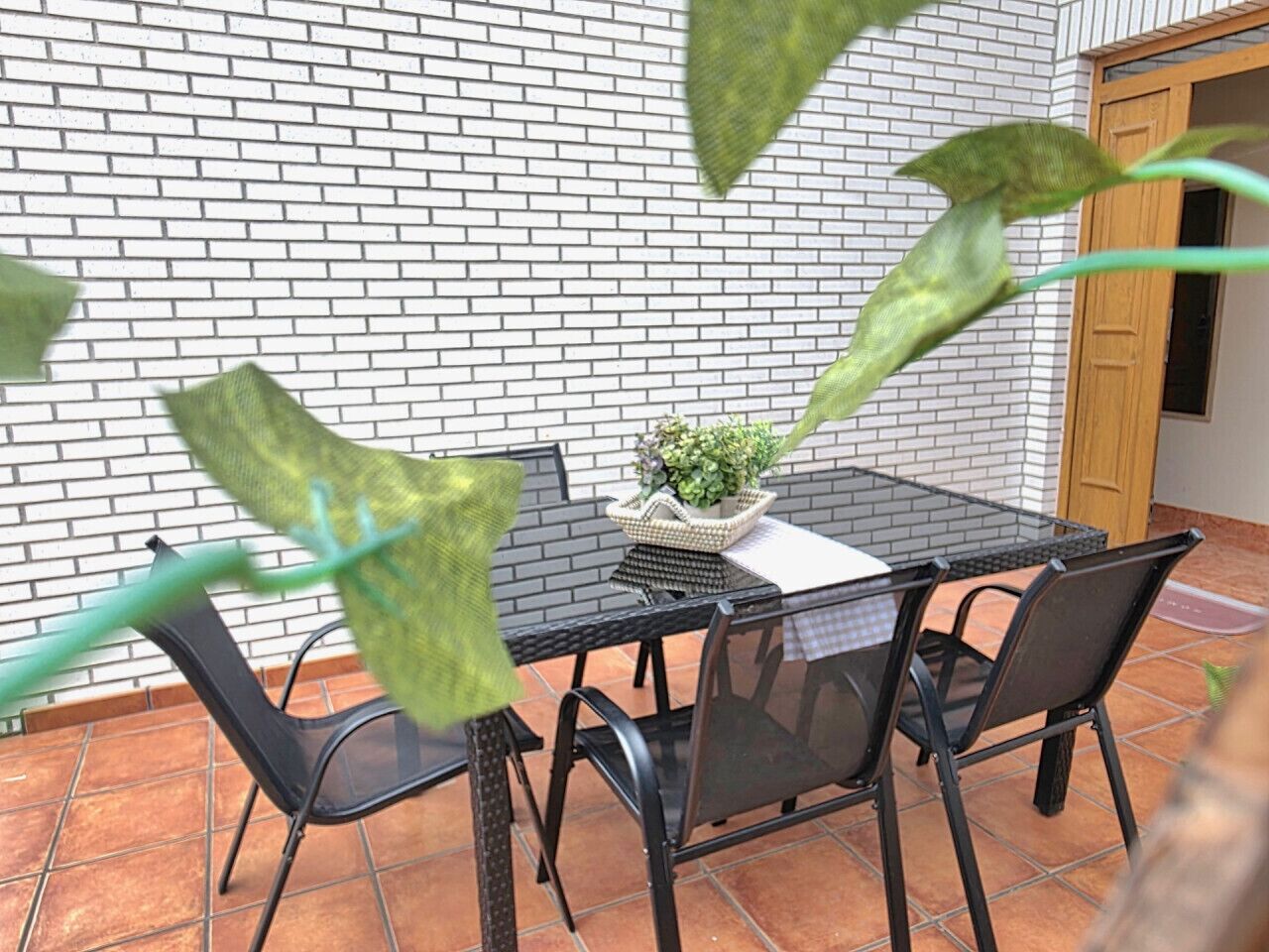 Eine Terrasse mit einem Glastisch, vier Stühlen, einem Blumentopf und einer Backsteinmauer.