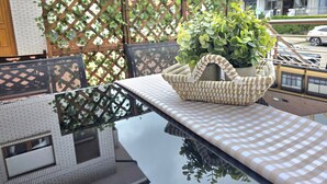 An outdoor dining area with a table and chairs, a woven basket with greenery, and a lattice fence in the background.