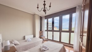 Une chambre d’hôtel avec deux lits, un lustre, une vue sur la mer et un balcon avec une chaise.