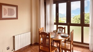 Un coin repas avec une table dressée pour quatre personnes, de grandes fenêtres avec des rideaux, un radiateur et un tableau encadré au mur.