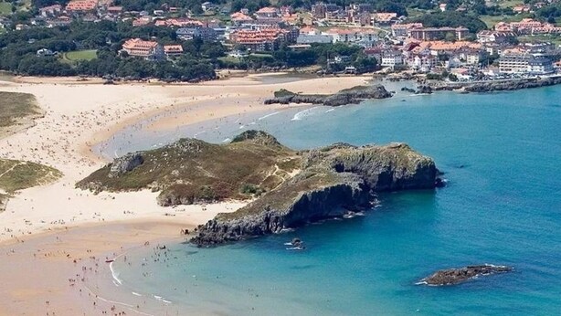 Une ville côtière avec une plage, des affleurements rocheux et des bâtiments en arrière-plan.