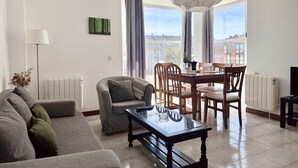 Una sala de estar moderna con un sofá, una mesa de comedor, sillas y un ventanal con cortinas.