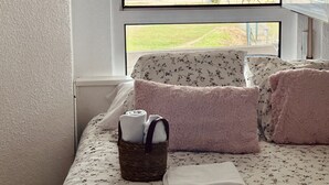 A bedroom with a bed, a window with a view of the sea, and a basket with towels. - Apto en primera línea - La Arena 4107 (Arnuero)
