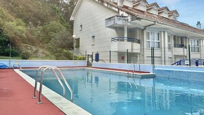 A swimming pool with metal ladders, a red deck, and a building with a tiled roof in the background. - Apto en primera línea - La Arena 4107 (Arnuero)