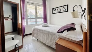 A hotel room with a bed, a desk, a chair, a window with curtains, and a wall with a framed picture. - Bajo en la playa con piscina - La Arena 4203 (Arnuero)