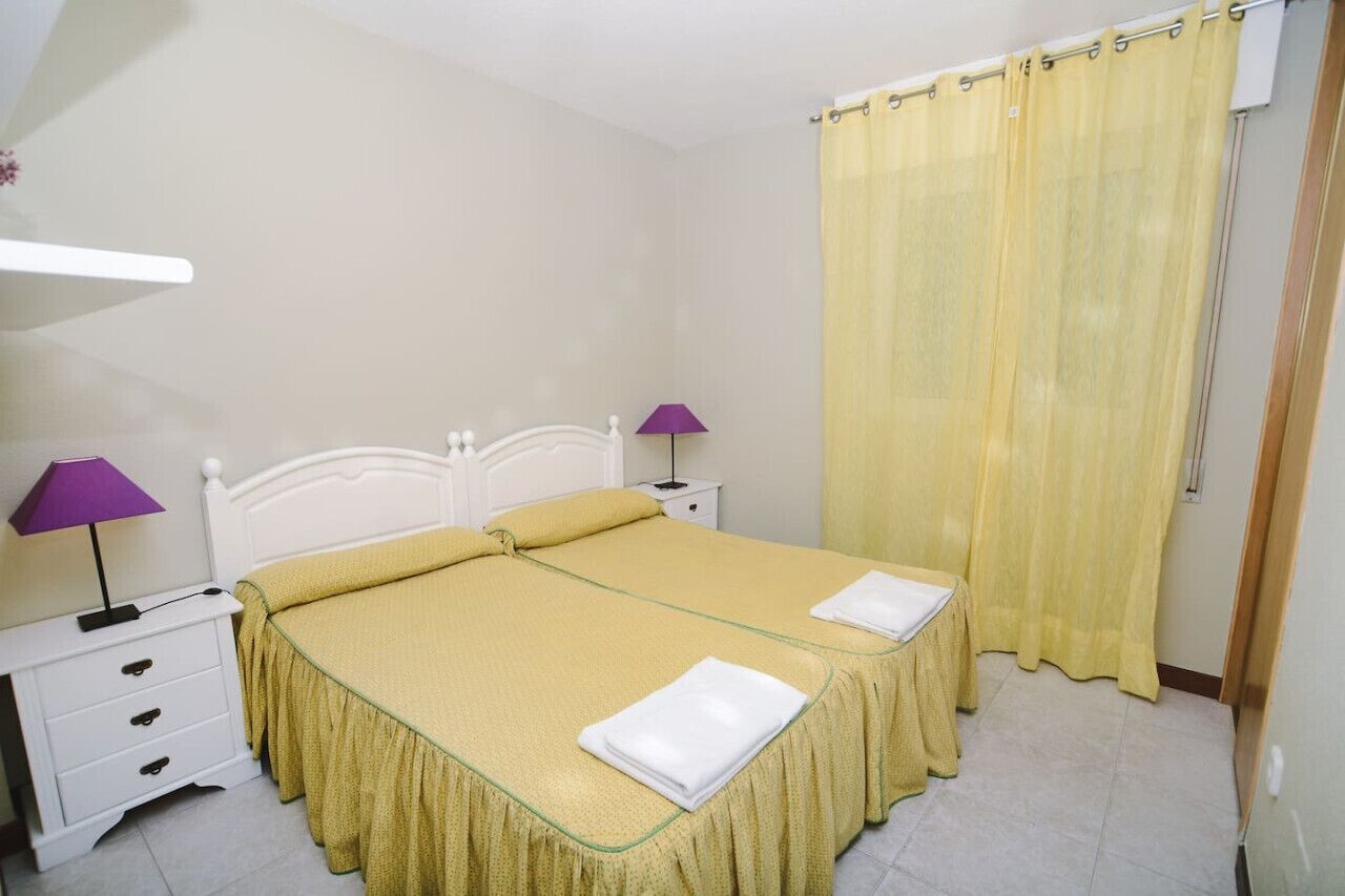 Un lit double avec une couvre-lit jaune, deux tables de chevet avec des lampes et un rideau jaune.