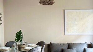 A modern living room with a glass dining table, grey sofa, and a woven pendant light.