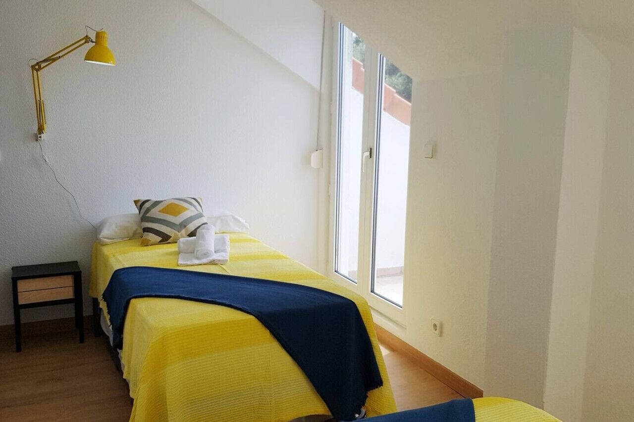 A bedroom with a bed, a bedside table, a lamp, and a window.