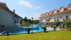 Ein Wohngebäude mit Schwimmbecken, umgeben von einer gepflegten Rasenfläche und wolkenlosem Himmel.