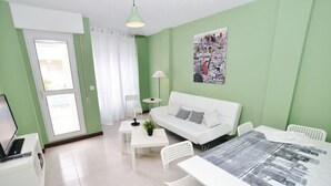 A modern living room with a white sofa, a dining table, and a cityscape artwork on the wall. - Apartamento con piscina en la playa-La Arena 4501 (Arnuero)