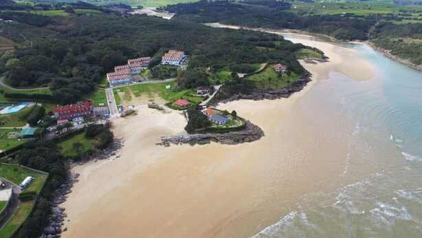 An aerial view of a coastal area with a beach, a river, and a residential complex with multiple buildings. - Apartamento con piscina en la playa-La Arena 4501 (Arnuero)