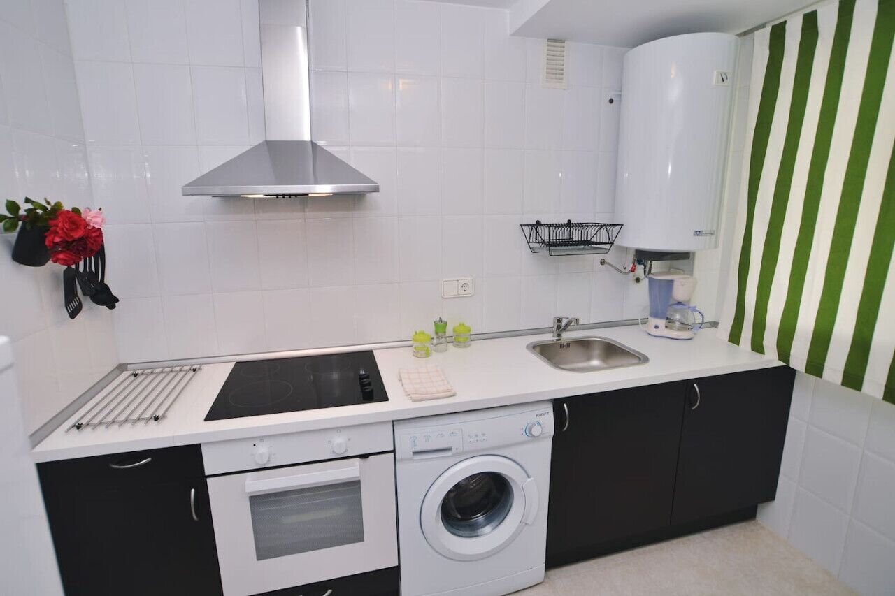 Une cuisine compacte équipée d’une cuisinière, d’un four, d’un lave-linge et d’un évier.