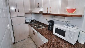 Una cocina compacta con armarios blancos, microondas, cafetera y pileta.