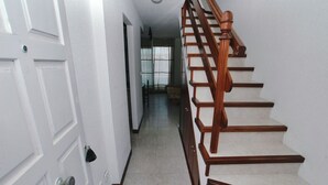 Un pasillo con una puerta blanca, una escalera de madera y vistas a una habitación con ventana.