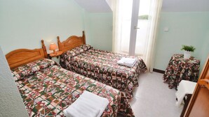 Un dormitorio con dos camas, una mesita, una lámpara y una ventana con cortinas.