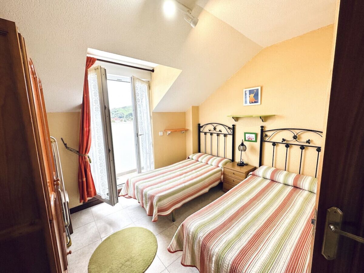 Une chambre avec deux lits, une fenêtre avec des rideaux, une petite table et une lampe fixée au mur.