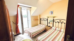 A bedroom with two beds, a window with curtains, a small table, and a wall-mounted lamp. - Apartamento con vistas - La Arena 4612 (Isla)