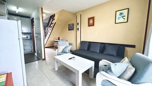 A modern living room with a sofa, a white coffee table, and a dining area with a refrigerator. - Apartamento con vistas - La Arena 4612 (Isla)