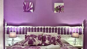 Een bed met een bloemenprint sprei, twee kussens, een bedlampje en een kleine plant op het nachtkastje.