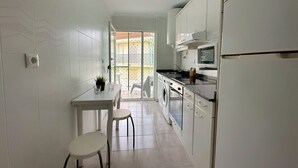 A compact kitchen with a washing machine, a dining area with a table and chairs, and a refrigerator. - Apartamento en Isla Playa - El Corrillo 5506 (Isla)