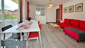 A modern living room with a red sofa, a dining table with red chairs, and a view of the outside through large windows. - Apartamento en Isla Playa - El Corrillo 5506 (Isla)