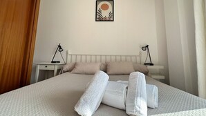 A neatly made bed with white linens and two pillows, a bedside table with a lamp, and a framed artwork on the wall. - Apartamento en Isla Playa - El Corrillo 5506 (Isla)