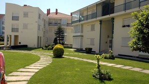 A courtyard with a pathway leading to a building with multiple balconies and a well-maintained lawn.