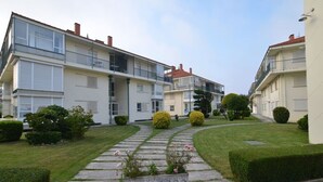 A row of modern apartment buildings with balconies, a well-maintained lawn, and a stone pathway leading to the entrance.