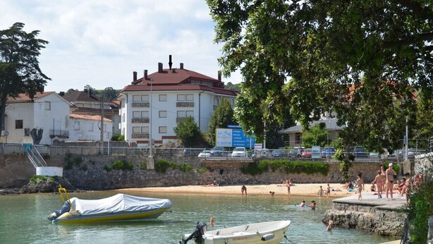 A coastal area with a sandy beach, a row of buildings, and several boats docked near the shore.