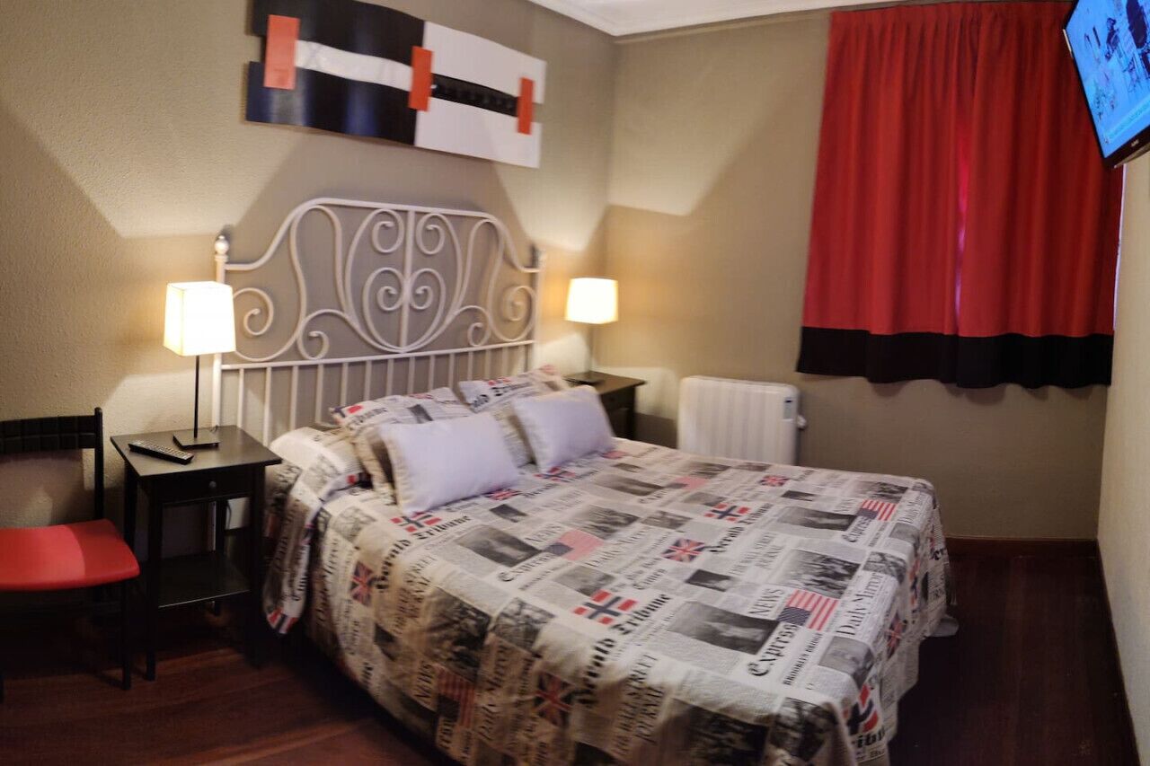 Una habitación de hotel con una cama, dos mesitas de noche con lámparas, una silla roja y una cortina roja.