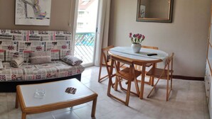 A living room with a sofa covered in newspapers, a round table with chairs, a vase with flowers, and a mirror on the wall. - Estudio en la Playa del Sable - El Corrillo 5602 (Arnuero)