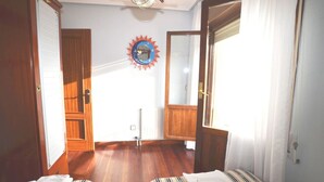A room with wooden flooring, a bed with striped bedding, a ceiling fan, and a wall-mounted clock.
